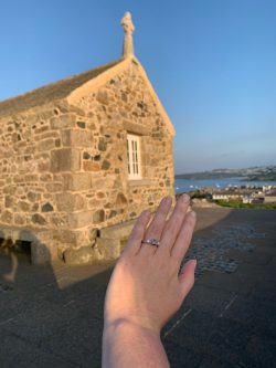 Platinum engagement ring with an oval sapphire and heirloom diamonds set either side with the St.Ives Island church in behind