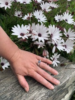 Platinum engagement ring with an oval sapphire and heirloom diamonds set either side with flowers