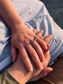 Platinum engagement ring with an oval sapphire and heirloom diamonds set either side holding hands with partner